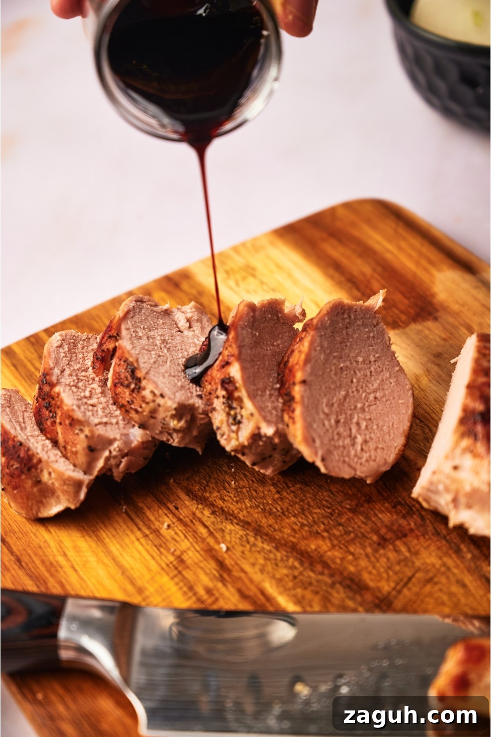 Juicy Sous Vide Pork Tenderloin Recipe — Perfectly Cooked Every Time 10 Close up of sliced and cooked pork tenderloin on a wood cutting board with a hand pouring a brown sauce over top the pork.