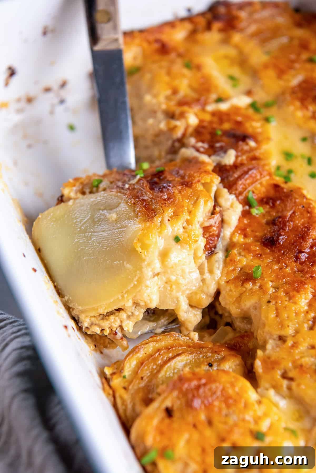 Creamy Scalloped Potatoes au Gratin Recipe 9 A spoon scoops au gratin potatoes from a baking dish.