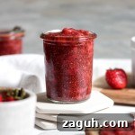 A glass jar of strawberry jam with fresh strawberries.