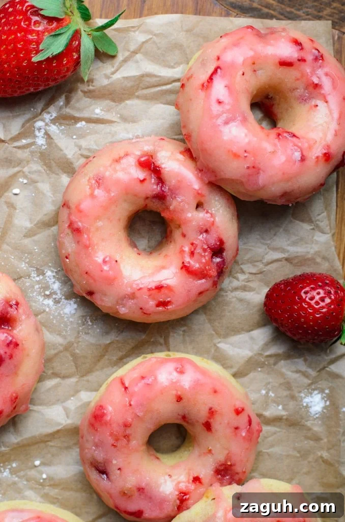 Strawberry-Glazed Baked Donuts: Light, Fruity Recipe 2 a batch of baked strawberry glazed donuts shown on crinkled brown parchment paper with fresh berries in the background