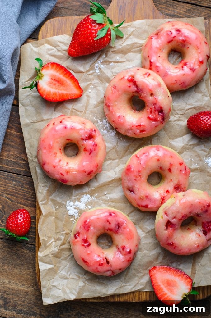 Strawberry-Glazed Baked Donuts: Light, Fruity Recipe 3 a batch of baked strawberry glazed donuts shown on crinkled brown parchment paper with fresh berries in the background