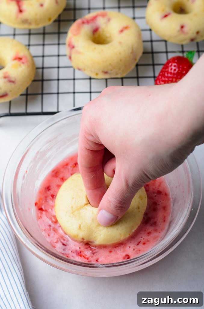 Strawberry-Glazed Baked Donuts: Light, Fruity Recipe 7 a hand shown dunking a strawberry donut into a bowl filled with pink glaze