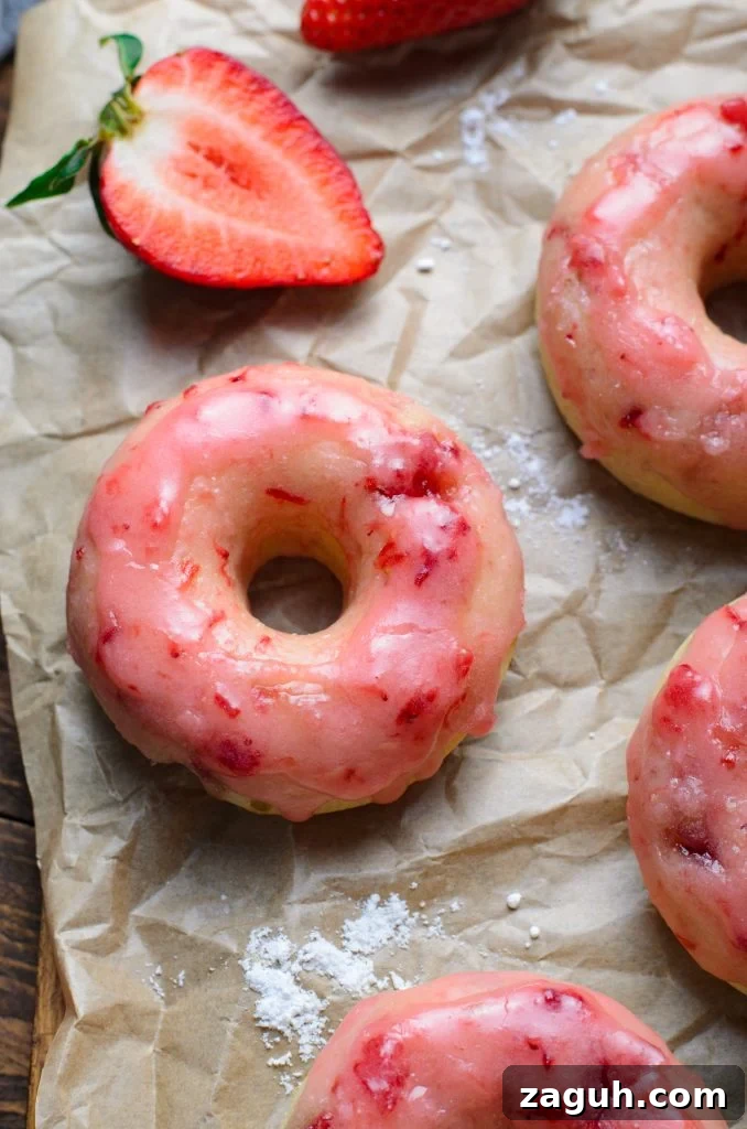 Strawberry-Glazed Baked Donuts: Light, Fruity Recipe 9 a batch of baked strawberry glazed donuts shown on crinkled brown parchment paper with fresh berries in the background