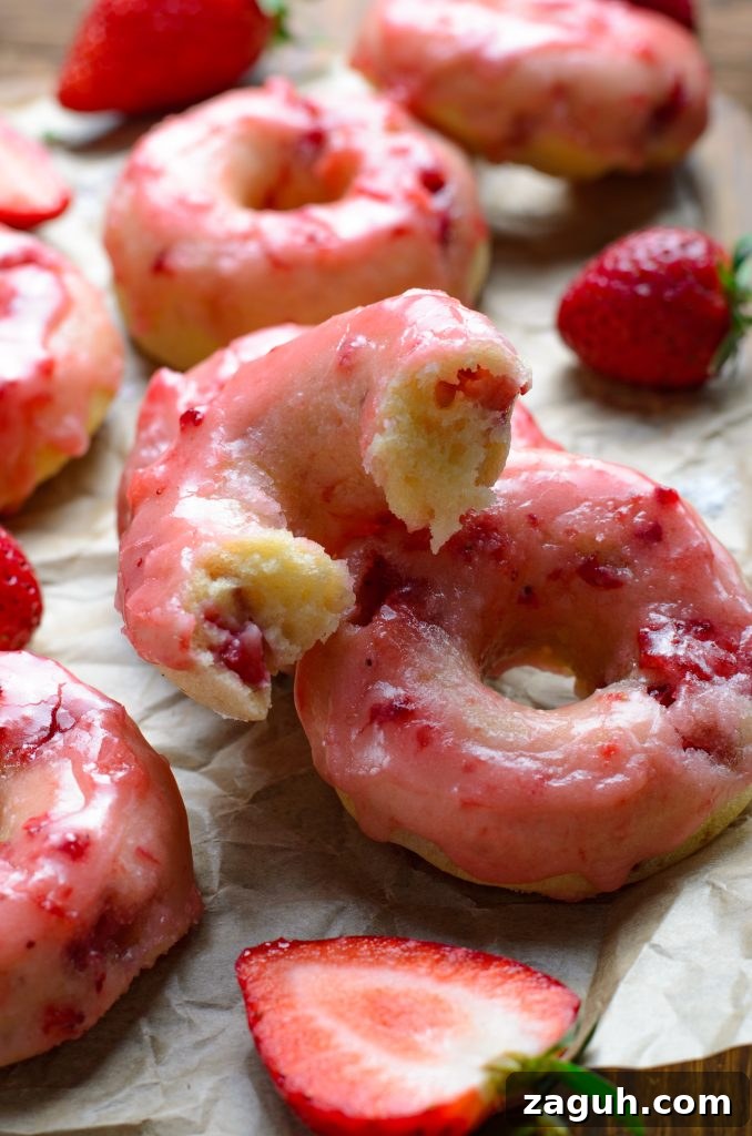Strawberry-Glazed Baked Donuts: Light, Fruity Recipe 10 a batch of baked strawberry glazed donuts shown on crinkled brown parchment paper with fresh berries in the background