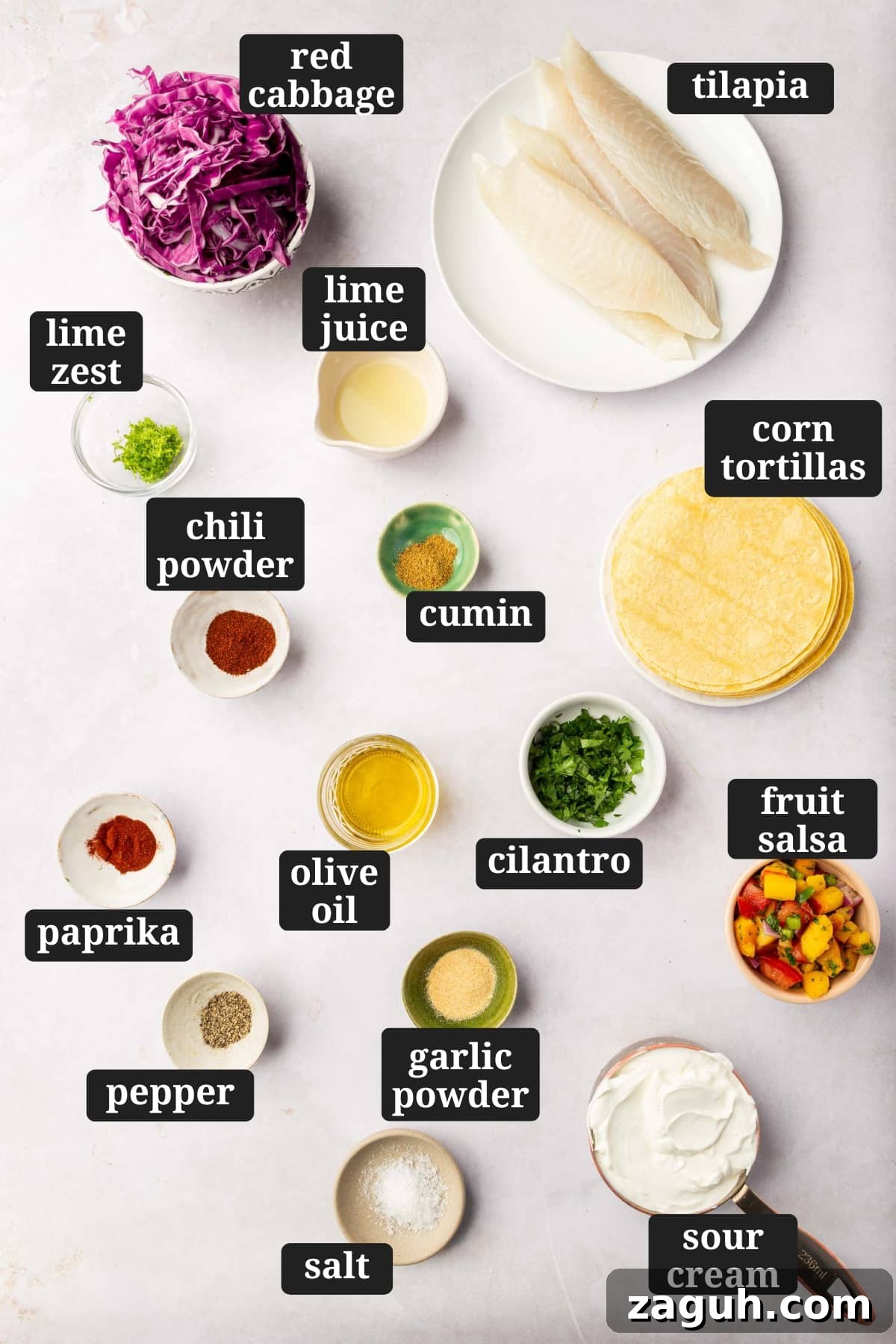 Crispy Tilapia Fish Tacos with Zesty Lime Slaw 3 Ingredients in small bowls to make tilapia fish tacos, including red cabbage, raw tilapia filets, lime zest, lime juice, cumin, paprika, chili powder, olive oil, cilantro, corn tortillas, pepper, garlic powder, salt, sour cream, and fruit salsa with text overlays over each ingredient.