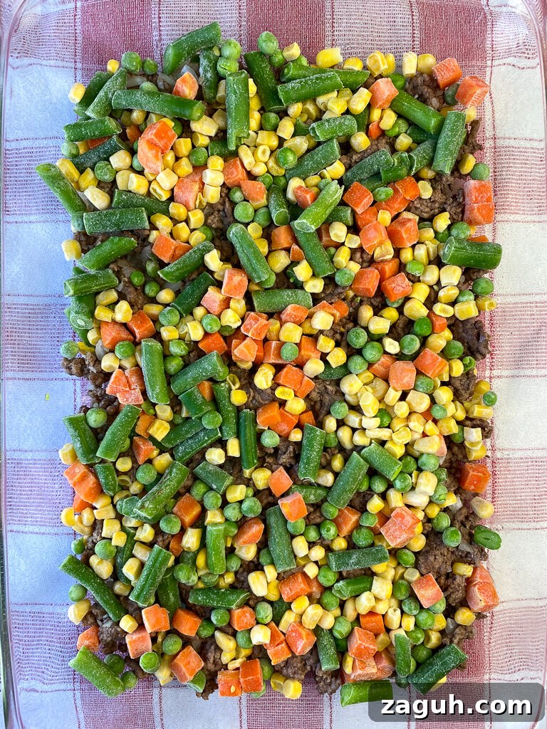 Cheesy Hamburger and Tater Tot Casserole Recipe That Families Love 9 Bag of frozen vegetables with green beans, corn, carrots and peans sprinkled on top of browned ground beef in a 9 x 13 dish