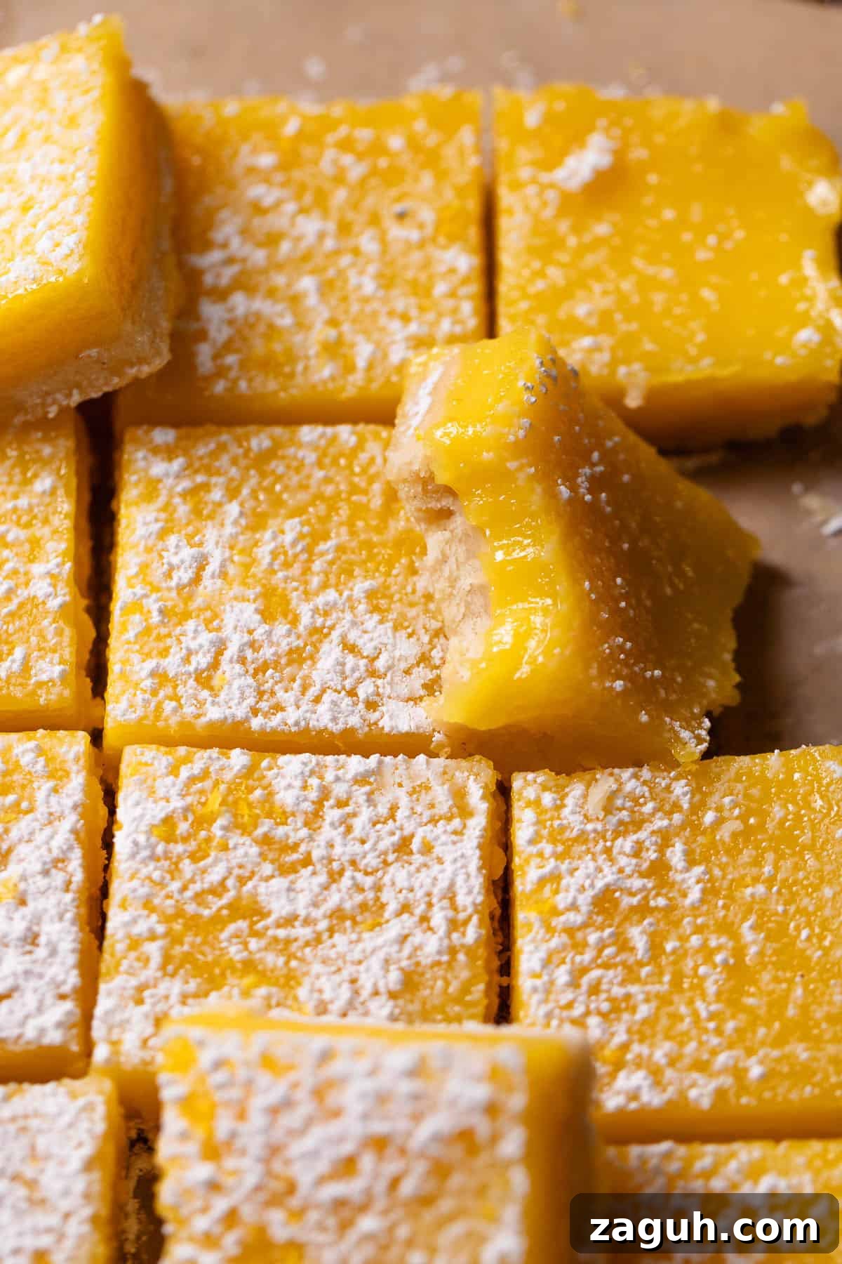 Tangy Lemon Bars with Buttery Shortbread Crust 2 Lemon bars dusted with powdered sugar with one missing a bite.