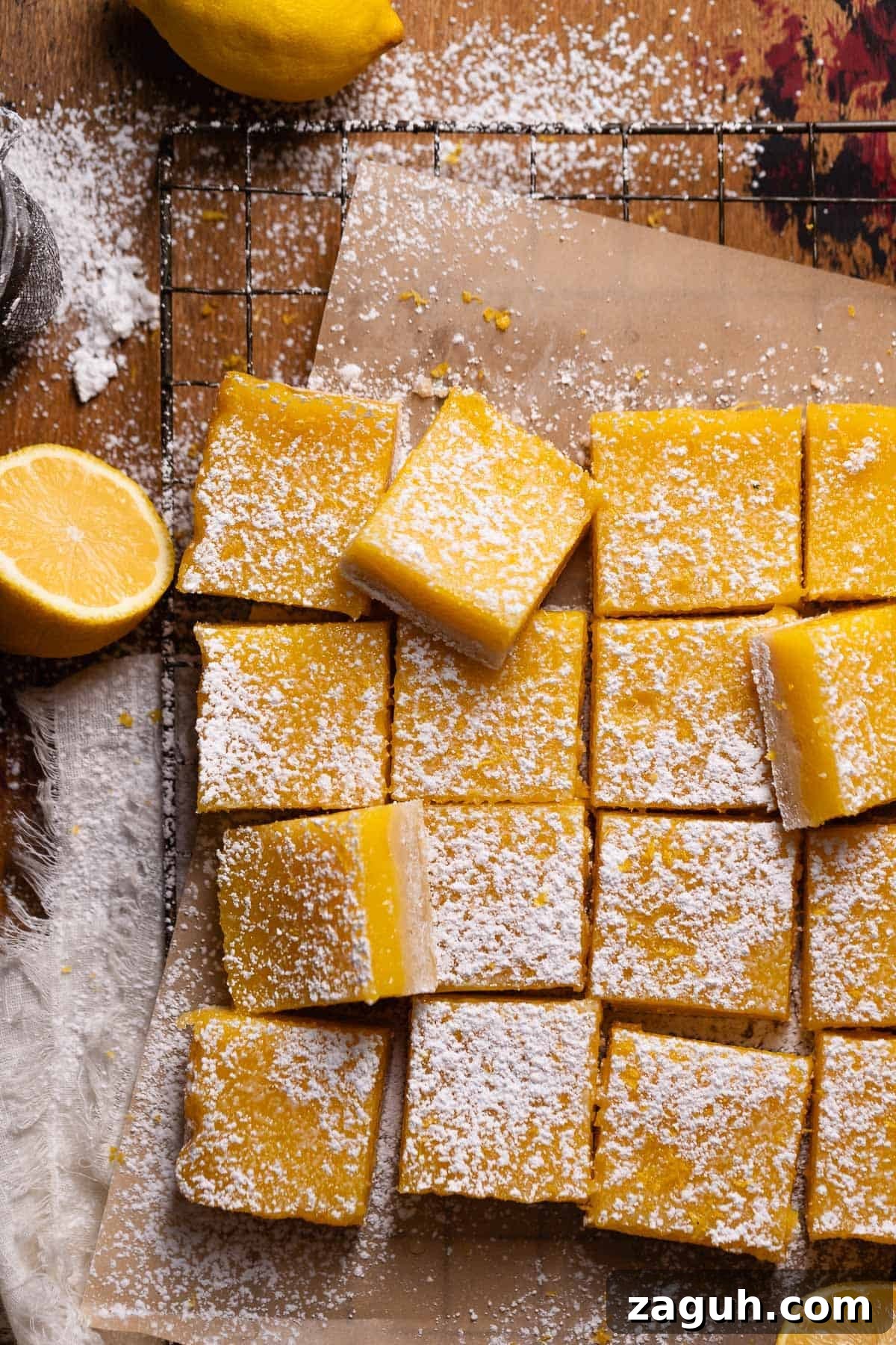 Tangy Lemon Bars with Buttery Shortbread Crust 9 Lemon bars cut into squares and dusted with powdered sugar on brown parchment paper.