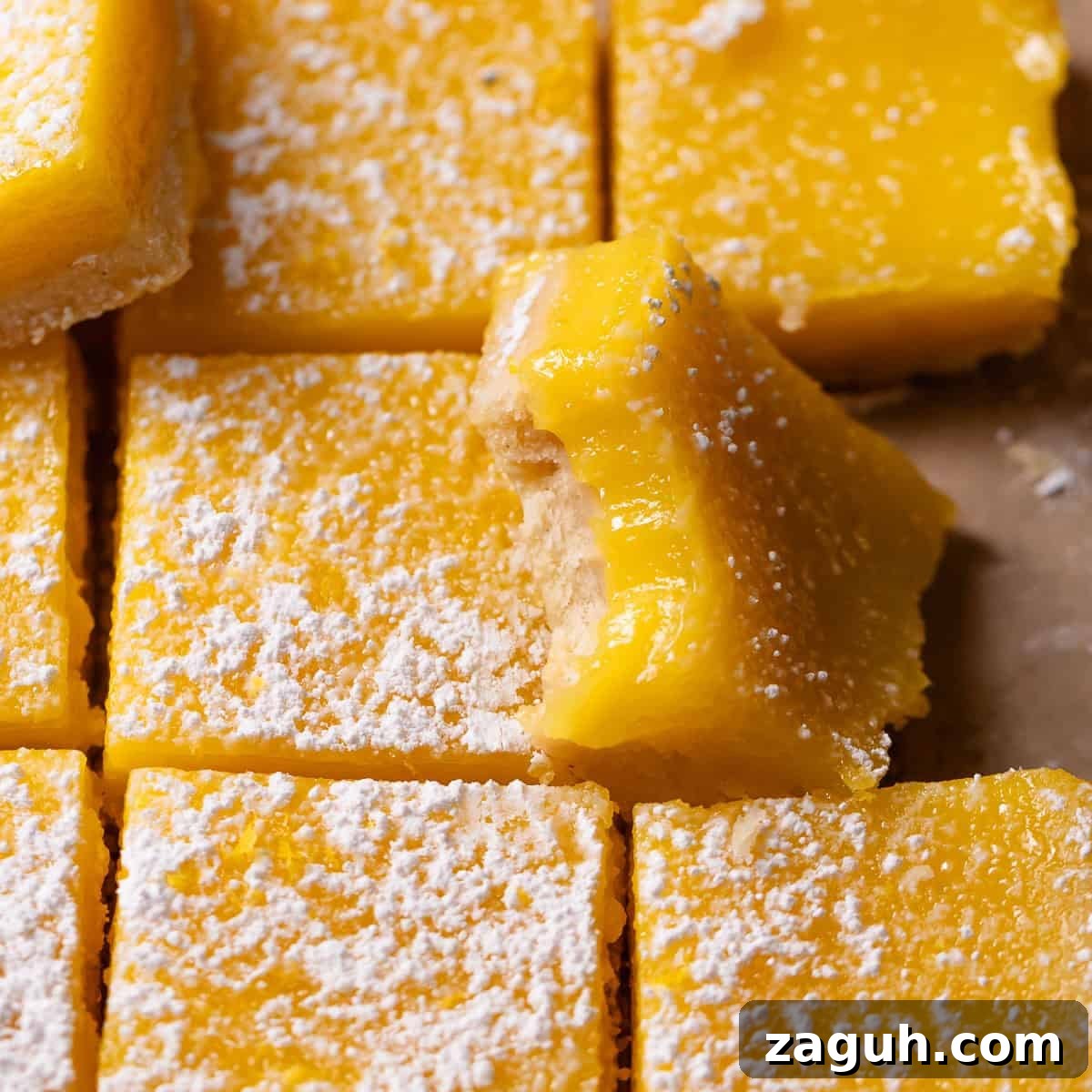 Tangy Lemon Bars with Buttery Shortbread Crust 10 Lemon bars dusted with powdered sugar with one missing a bite.
