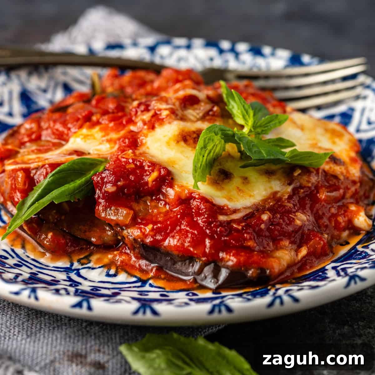 Classic Eggplant Parmigiana Recipe: Authentic Italian Parmigiana di Melanzane 2 closeup side view: eggplant parmigiana on blue and white plate with fork