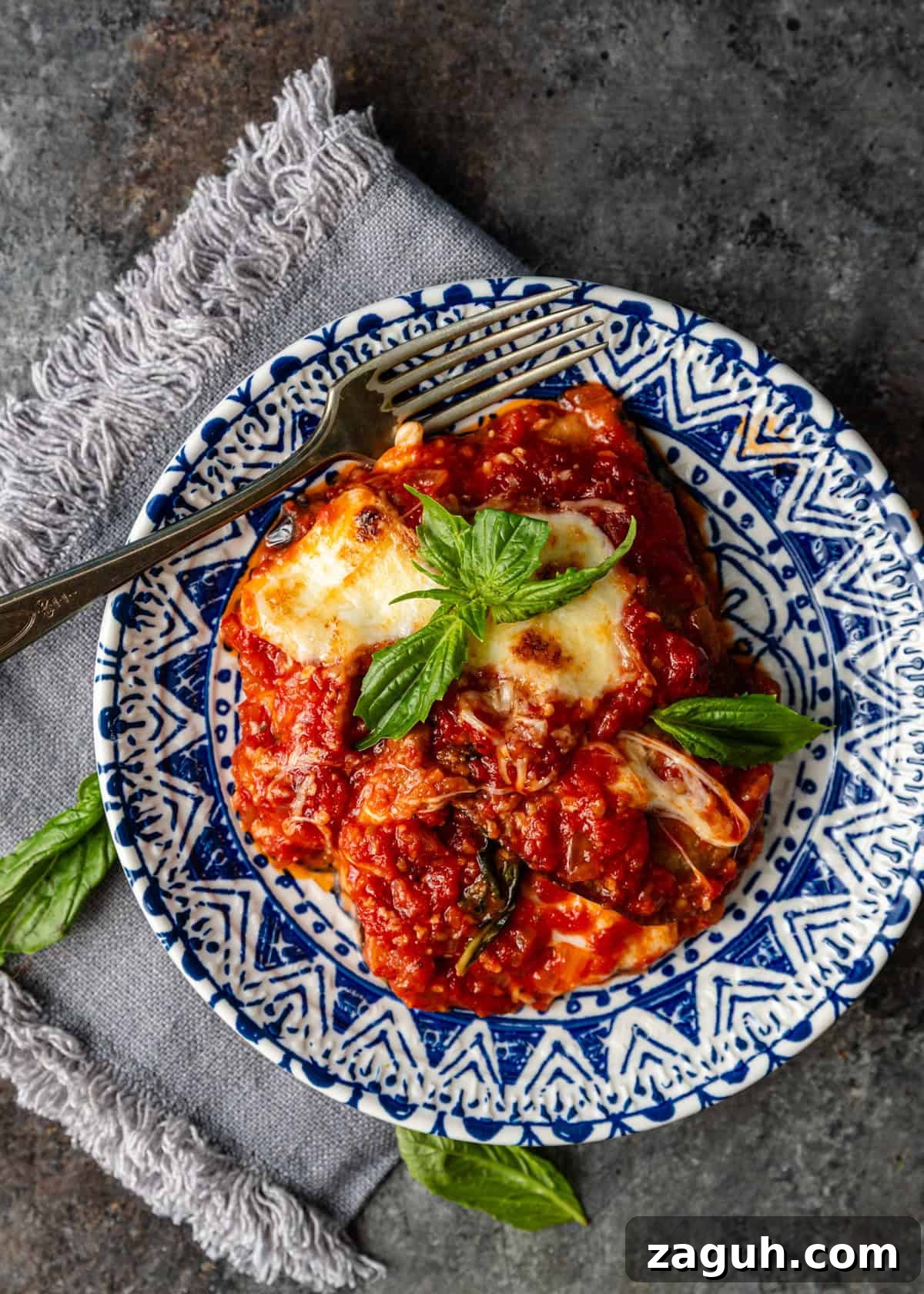 Classic Eggplant Parmigiana Recipe: Authentic Italian Parmigiana di Melanzane 14 overhead: a big slice of parmigiana on white and blue plate topped with basil and fork on side