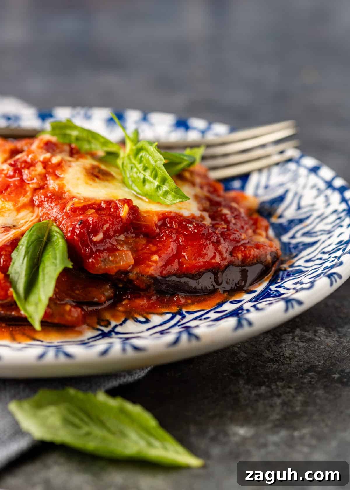 Classic Eggplant Parmigiana Recipe: Authentic Italian Parmigiana di Melanzane 3 closeup side view: parmigiana on blue and white plate with basil on top