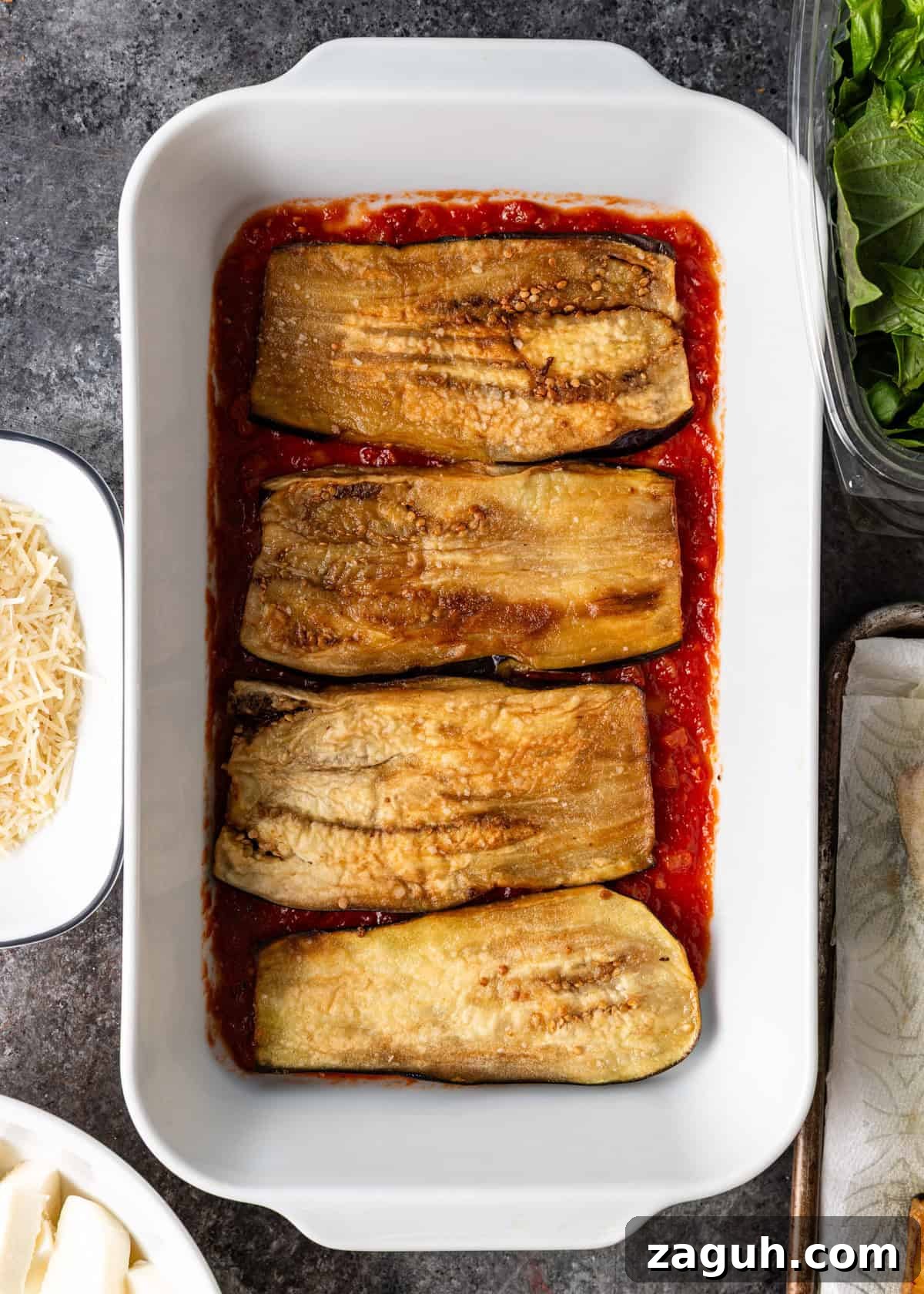 Classic Eggplant Parmigiana Recipe: Authentic Italian Parmigiana di Melanzane 10 overhead process shot: white baking dish with sauce on bottom, layered with egg plant