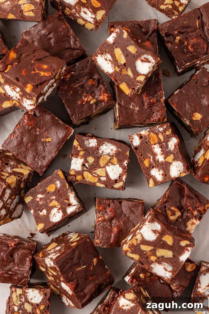 Squares of chocolate fudge filled with chopped nuts and mini marshmallows are arranged closely together on a light surface, showing the mix of ingredients inside each piece.