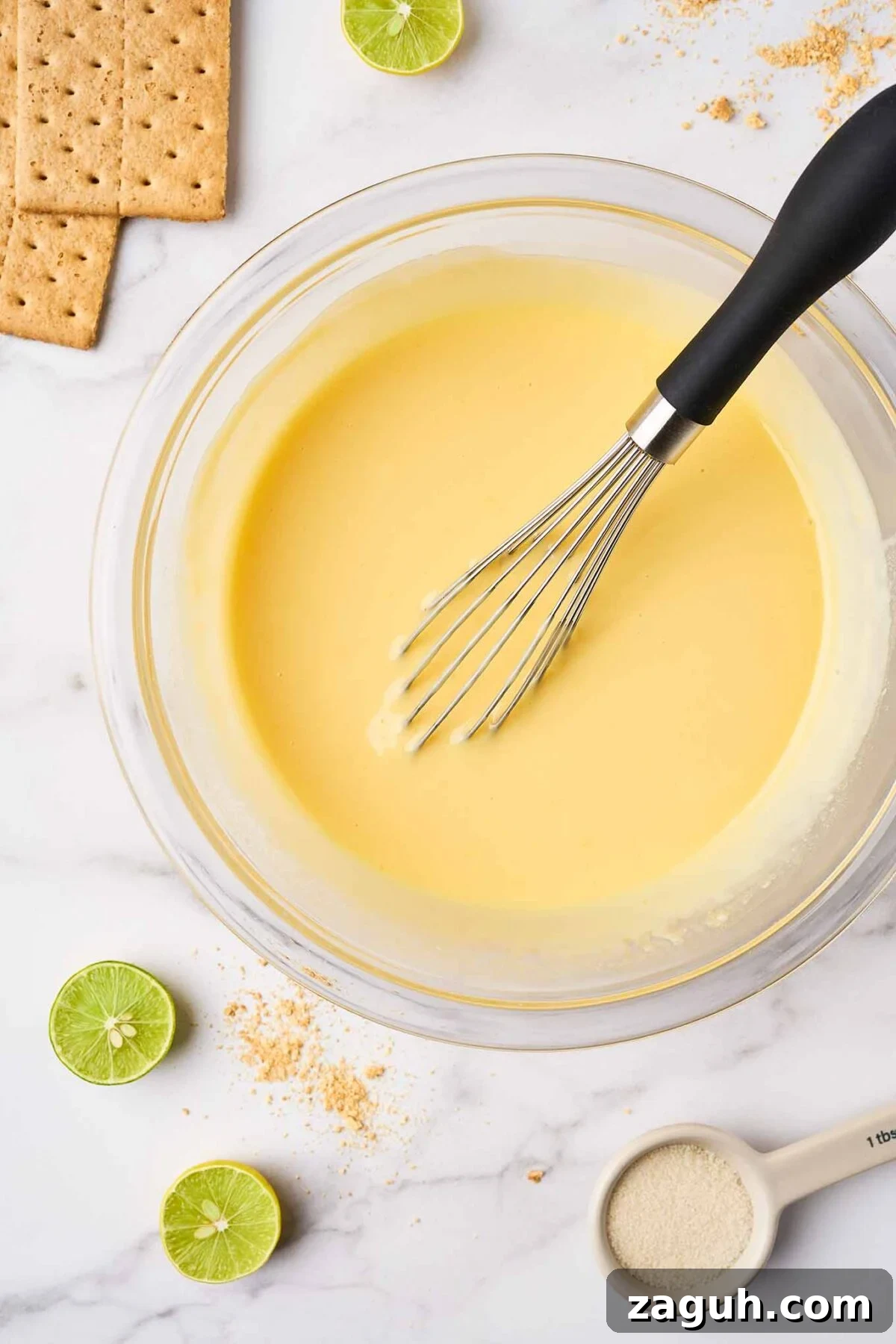 Key lime pie filling made with egg yolks, lime juice, and sweetened condensed milk being whisked in a bowl.