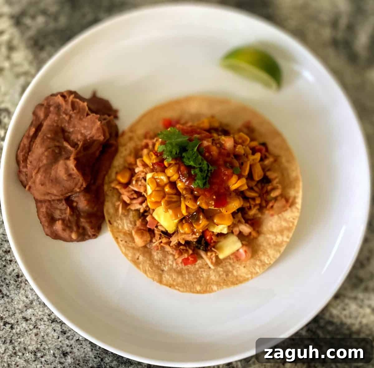 Jackfruit Carnitas: Flavorful Vegan Pulled Pork Tacos 10 Jackfruit carnitas recipe served on corn tortillas with corn salsa, pineapple, cilantro with a side of refried beans on a plate.