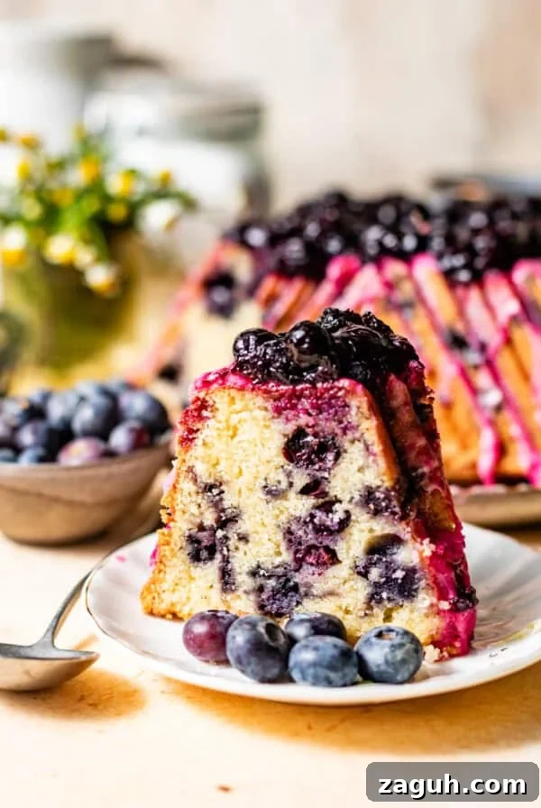 Moist Corn Pound Cake Recipe with Creamy Cornmeal Crumble 14 a slice of lemon blueberry pound cake on a cake plate topped with blueberry lemon glaze and blueberry compote on top.
