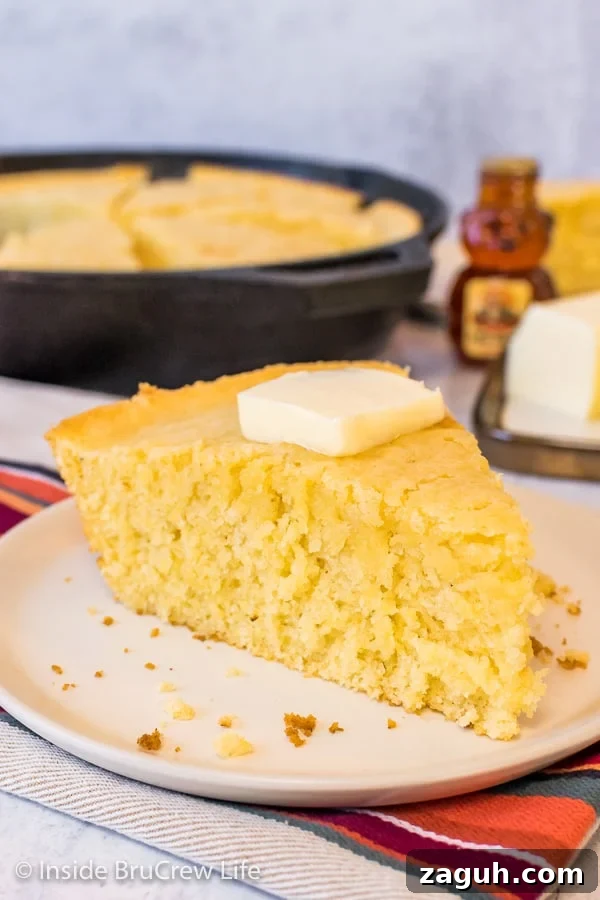 Easy Skillet Cornbread - a pan of this easy cornbread comes together in minutes with ingredients from your pantry. Great recipe to make and serve with chili, soup, or pork. A wedge of skillet cornbread on an off white plate with the skillet behind it