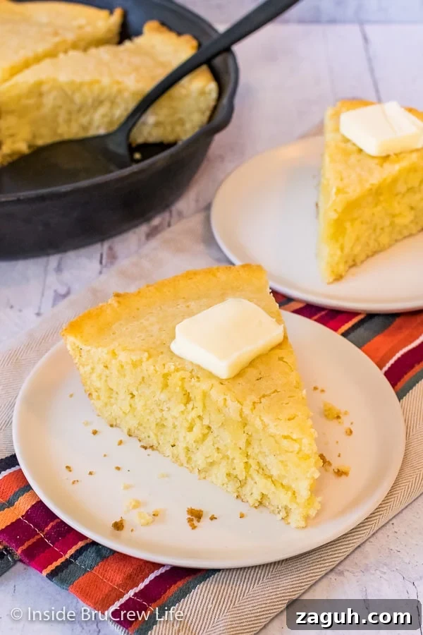 Easy Skillet Cornbread - a pan of cornbread is easy to make with simple ingredients from your pantry. Great recipe to make and serve with chili, pork, or soups. Slightly overhead picture of a wedge of skillet cornbread with a pat of butter on an off white plate