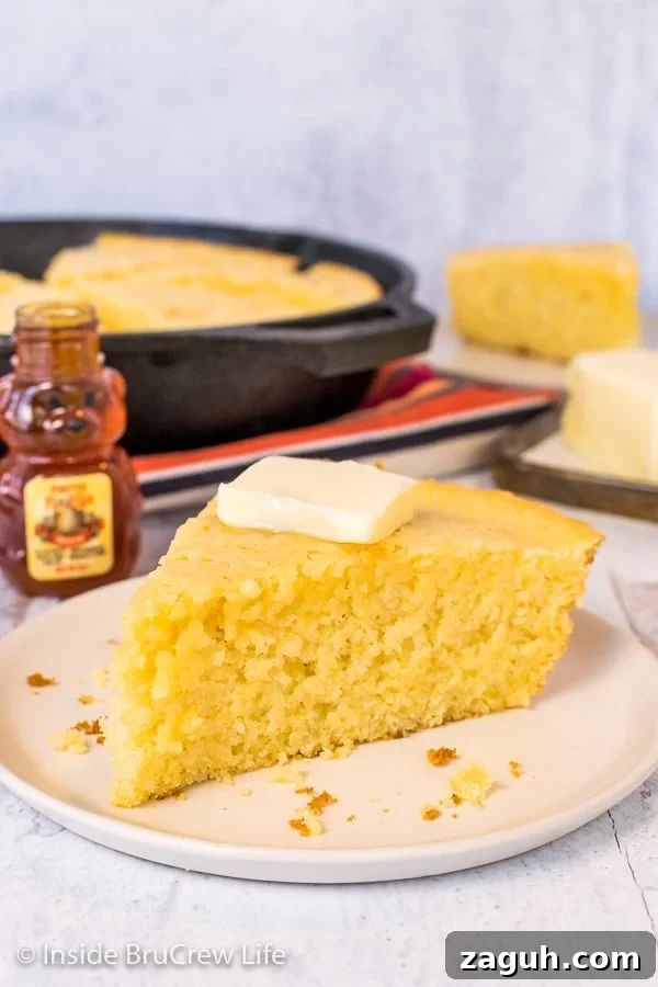 Easy Skillet Cornbread - make this easy cornbread with simple ingredients from your pantry. It is a great recipe to serve with chili, pork, or soups. A wedge of easy cornbread with a pat of butter on an off white plate with a skillet of cornbread behind it