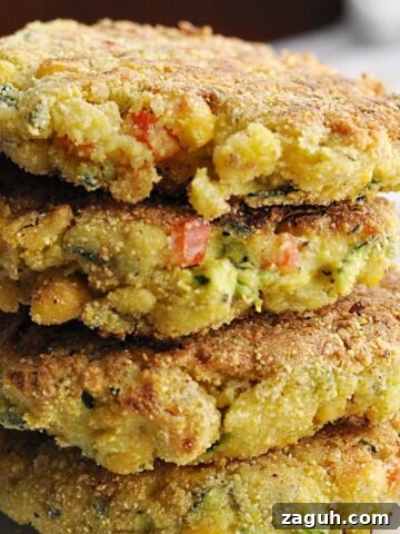 Four corn zucchini fritters with red peppers stacked on plate.