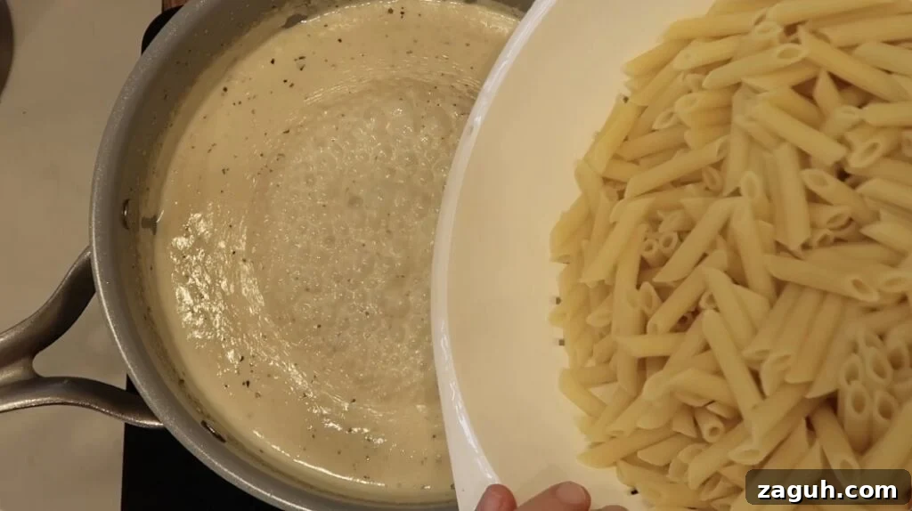 Creamy Garlic Sauce Recipe for Pasta, Chicken, and Veggies 15 Adding pasta to pan with sauce in it