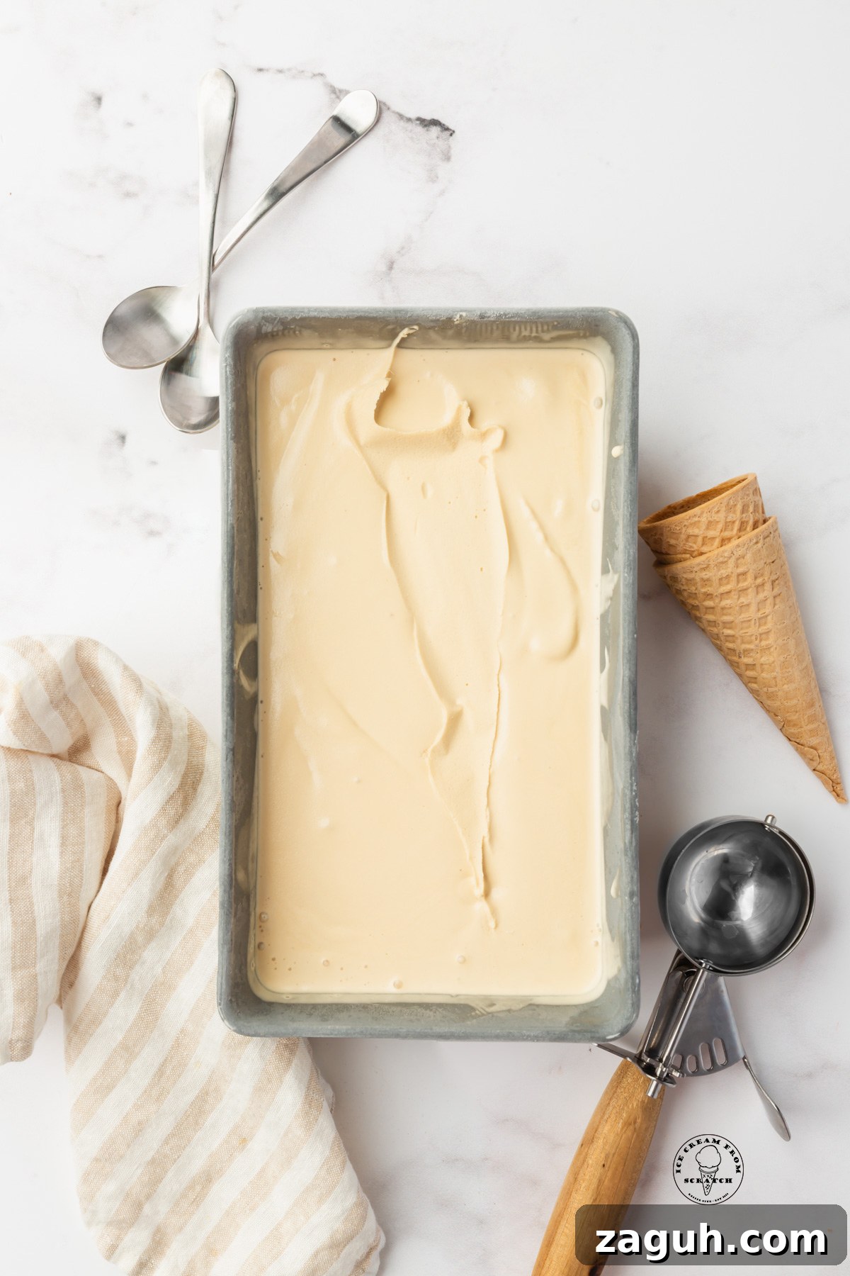 Homemade caramel ice cream in a metal loaf pan. an ice cream scoop and sugar cones are next to the pan.