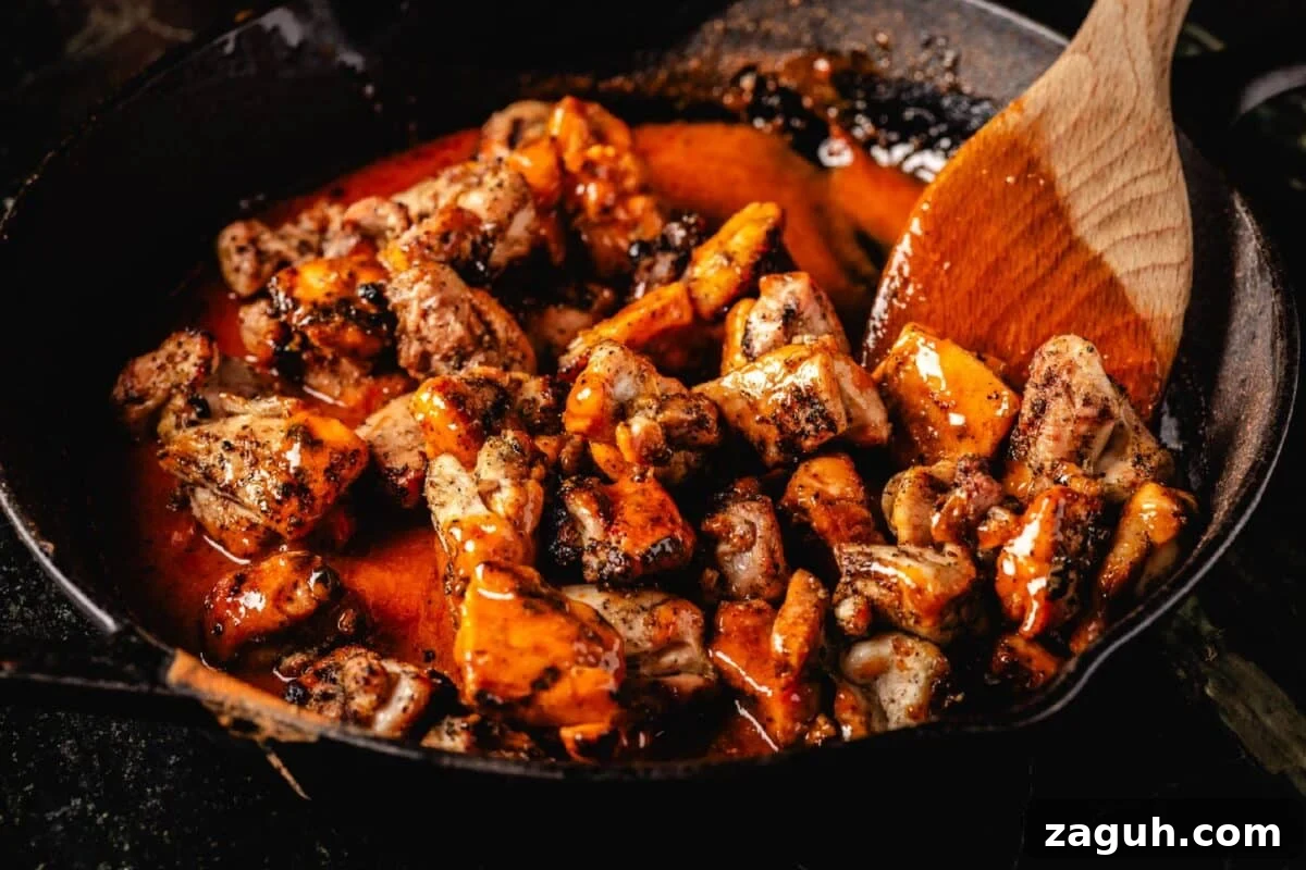 Grilled Buffalo Chicken Bites: Spicy BBQ Chicken Skewers 6 Chicken thighs being mixed into buffalo sauce in skillet with wooden spoon.