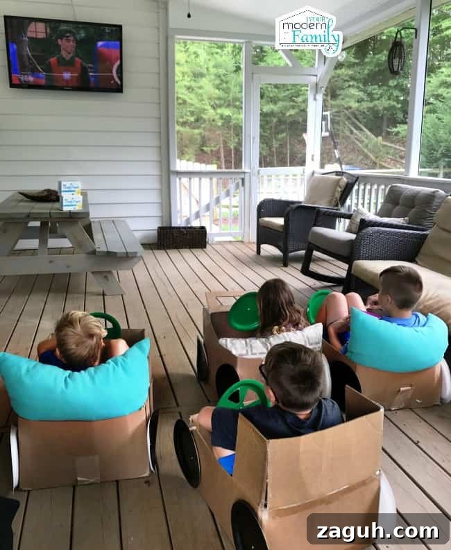 A group of kids sitting in homemade cardboard cars watching television on a porch.