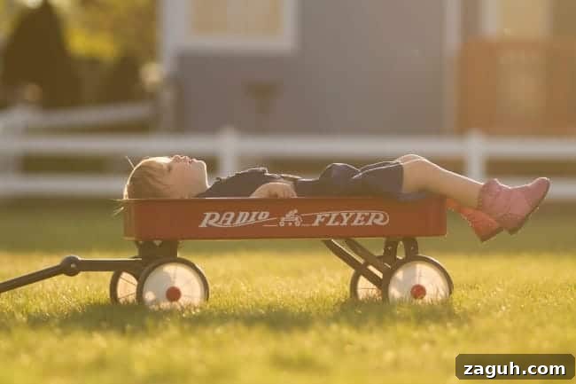 A young boy lying on a red wagon looking up to the sky.