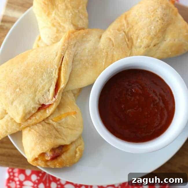 A plate of pepperoni pizza twists and a cup of red sauce.