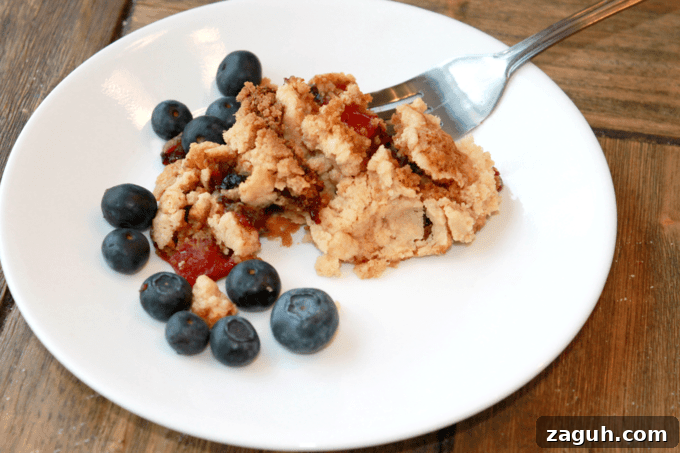 A baked scoop of Dump Cake on a white plate with blueberries around it.
