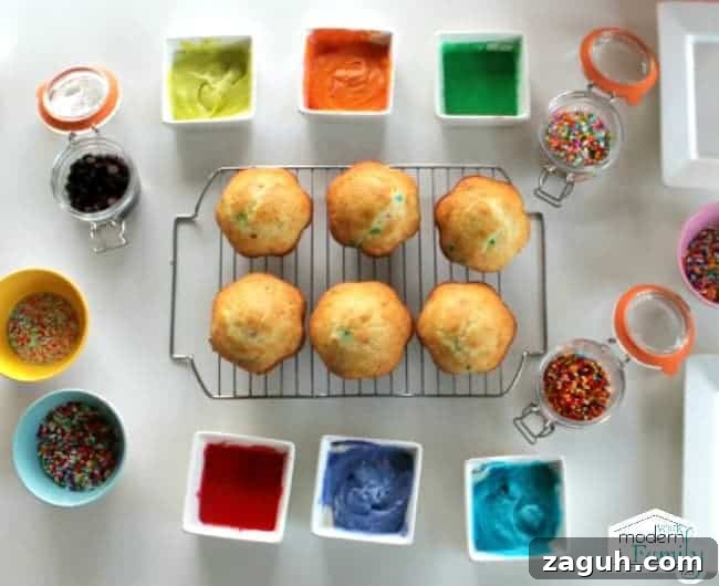 Cupcakes resting on a wire rack with a variety of icings and sprinkles in cups all around them.