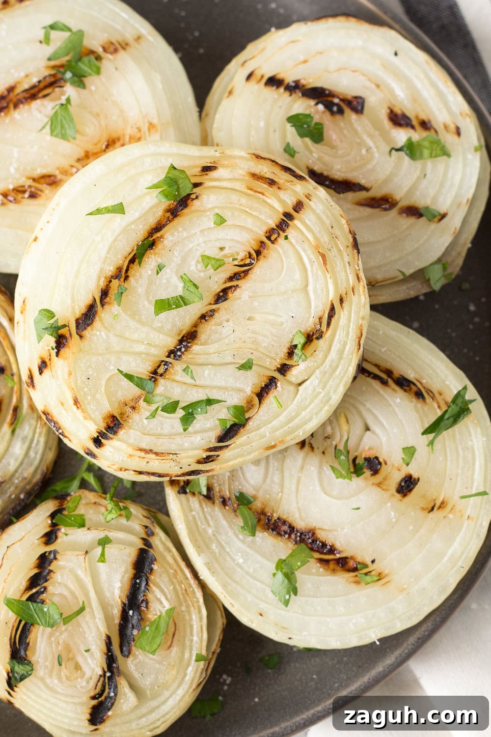 Grilled Onions Recipe: Whole30, Paleo & Gluten-Free Side Dish 2 Close up of grilled onions on a gray plate sprinkled with salt and chopped fresh parsley.
