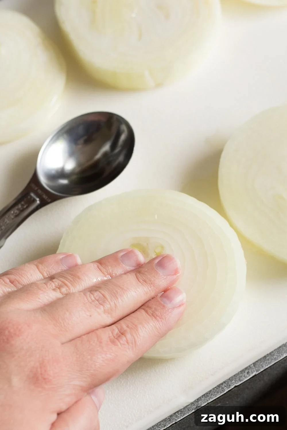 Grilled Onions Recipe: Whole30, Paleo & Gluten-Free Side Dish 6 A hand rubbing oil into a large slice of onion on a white cutting board.