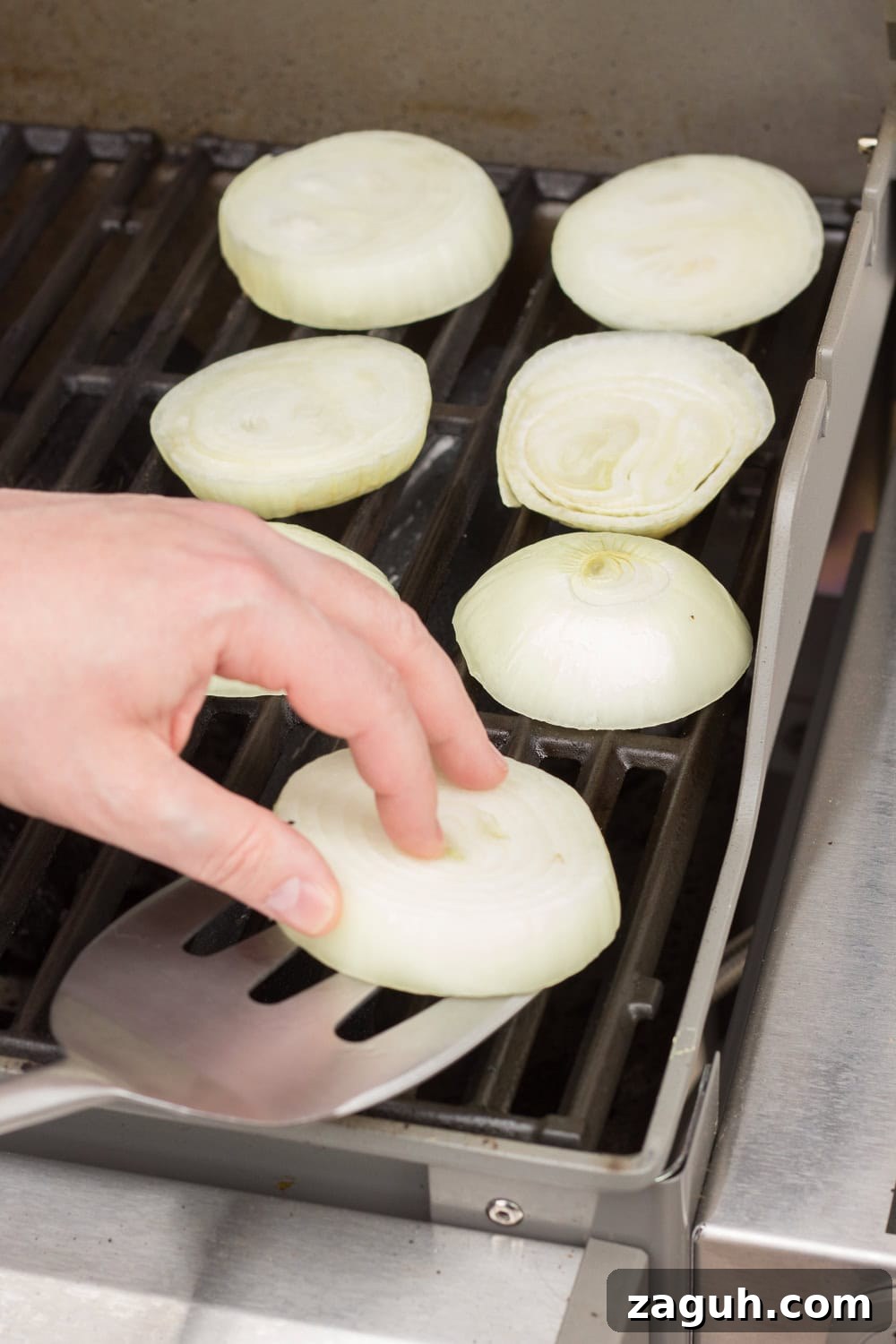 Grilled Onions Recipe: Whole30, Paleo & Gluten-Free Side Dish 7 A hand placing an onion ring on a grill. Six other slices of onion are on the grill beside it.