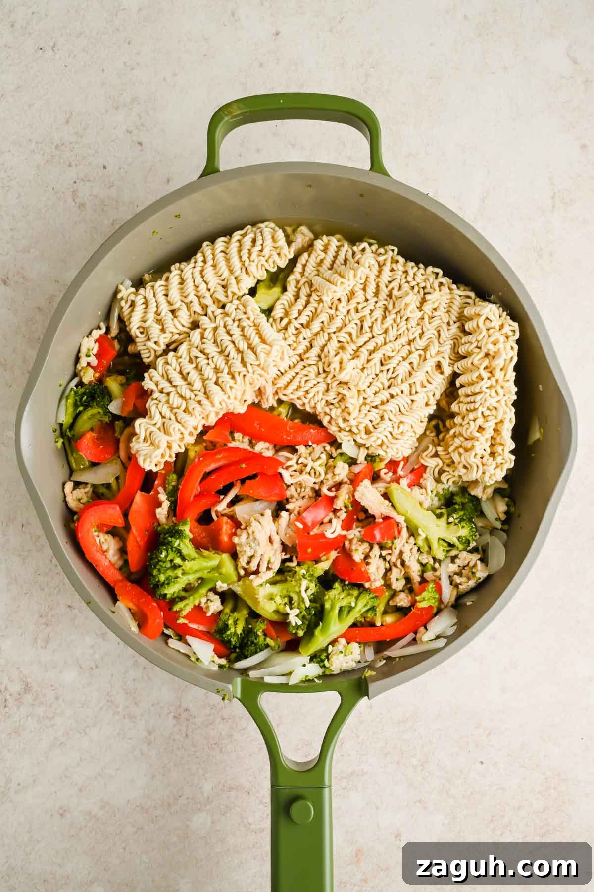 cooked veggies and ground chicken in skillet with raw ramen noodle blocks.