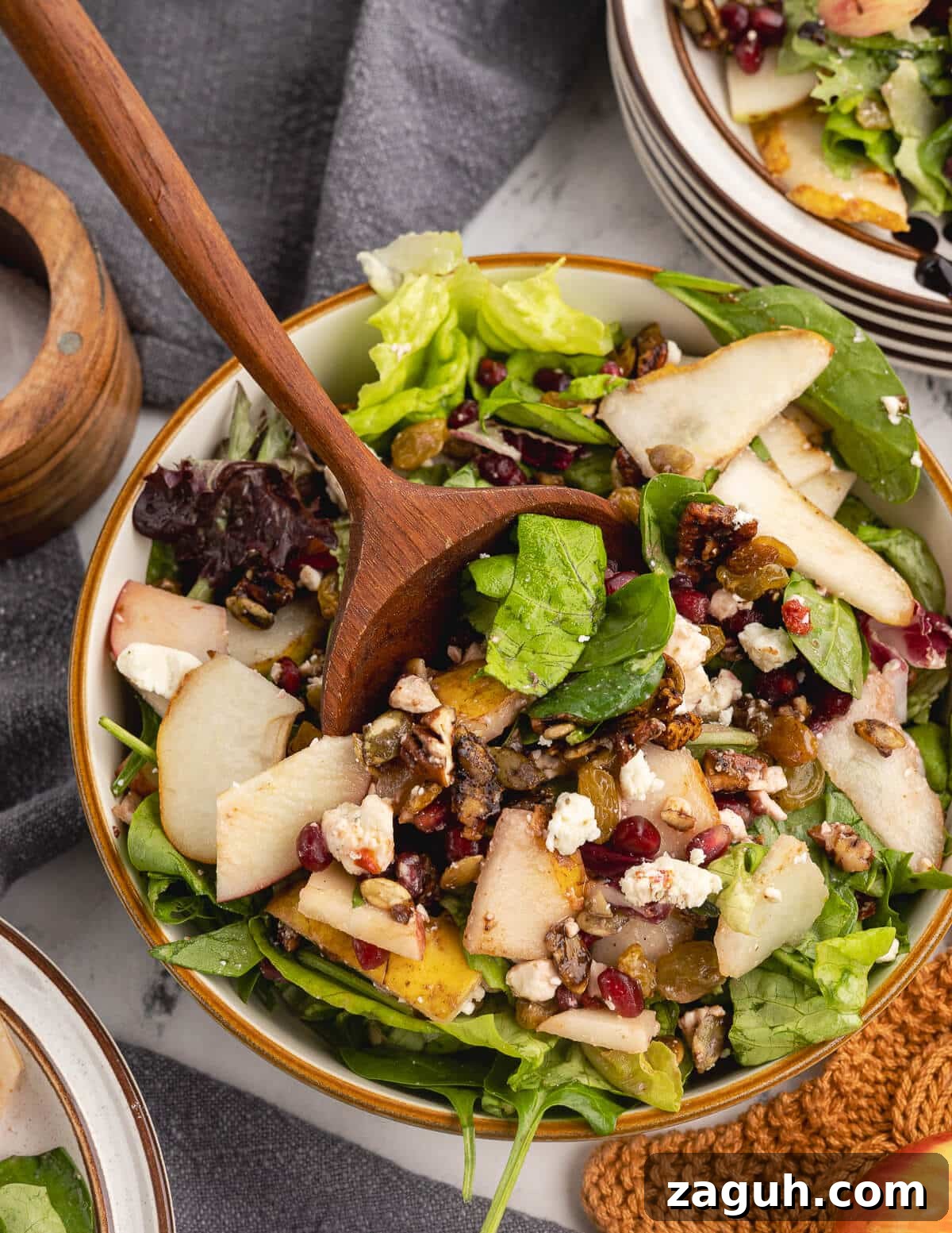 Pomegranate, Pear & Candied Pepita Salad with Citrus Vinaigrette 12 a salad with a wooden spoon in it with pears, feta, pomegranate seeds, and candied pepitas.