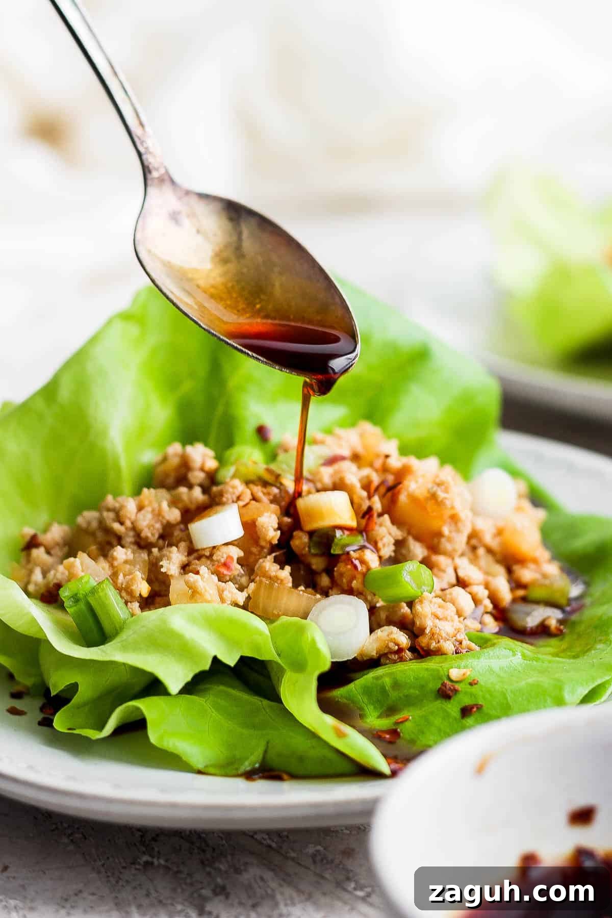 Savory Chicken Lettuce Wraps with Asian Hoisin Sauce 9 A spoon pouring more sauce on top of a chicken lettuce wrap.