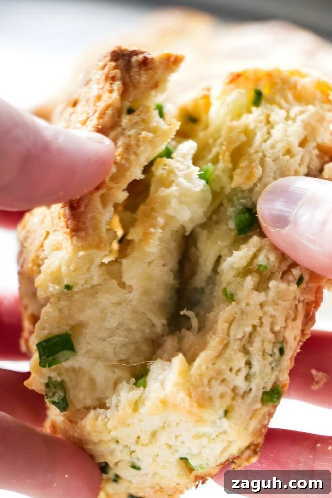 Hands break open a flaky biscuit with green onions.