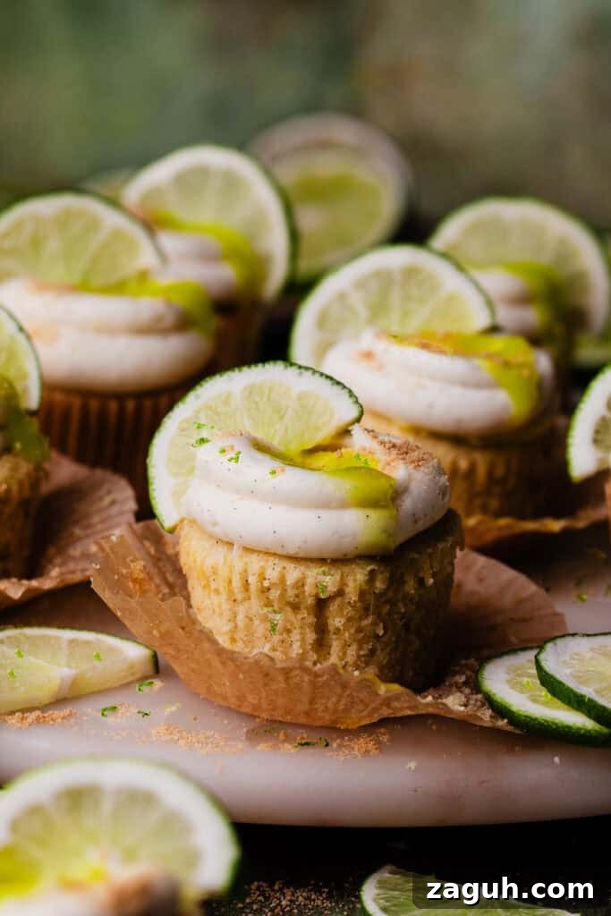 Key Lime Cupcakes with Tangy Lime Curd Filling 2 Key Lime Cupcakes on a marble cake plate, topped with swirls of cream cheese frosting, lime curd, and a lime slice for garnish.