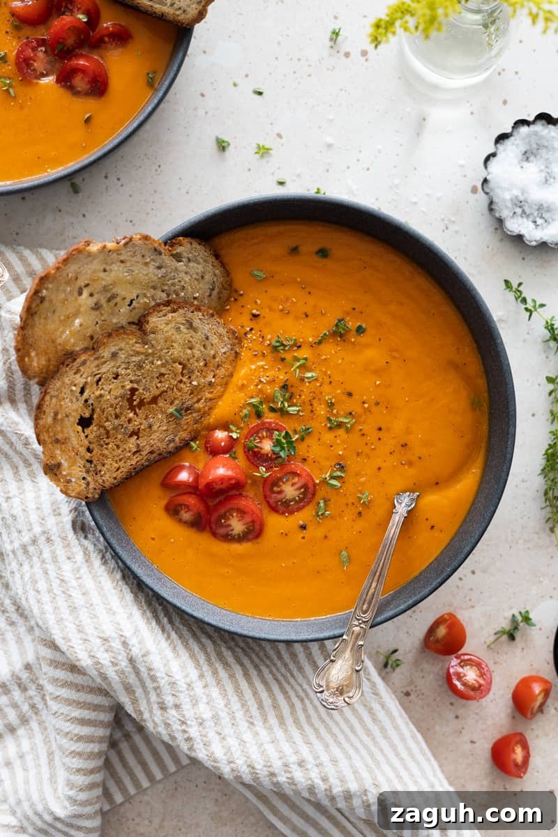 Roasted Butternut Squash and Red Pepper Soup Recipe 2 Butternut squash and red pepper soup in a grey bowl with two slices of crispy bread, halved cherry tomatoes and fresh thyme.