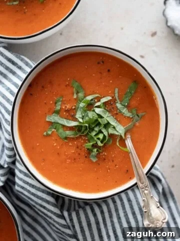 Roasted red pepper and tomato soup on a bowl with a spoon.