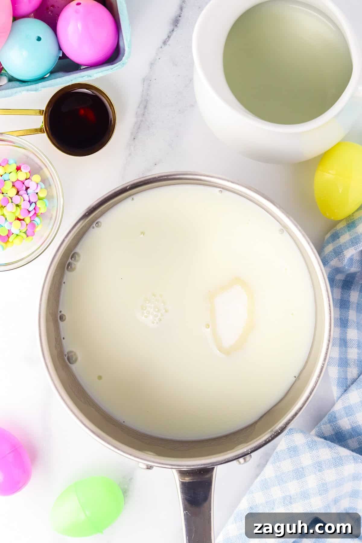How to Make Copycat Cadbury Creme Egg Candy at Home 6 A pot of hot milk on a kitchen counter surrounded by ingredients for baking a copycat Creme Egg candy.
