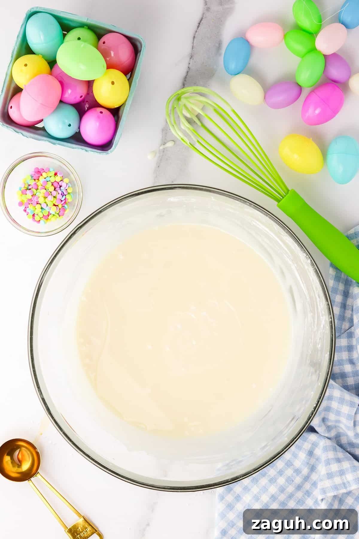How to Make Copycat Cadbury Creme Egg Candy at Home 9 Ingredients and utensils for Easter baking, featuring colorful plastic eggs, Creme Egg Candy, and cake batter on a kitchen countertop.