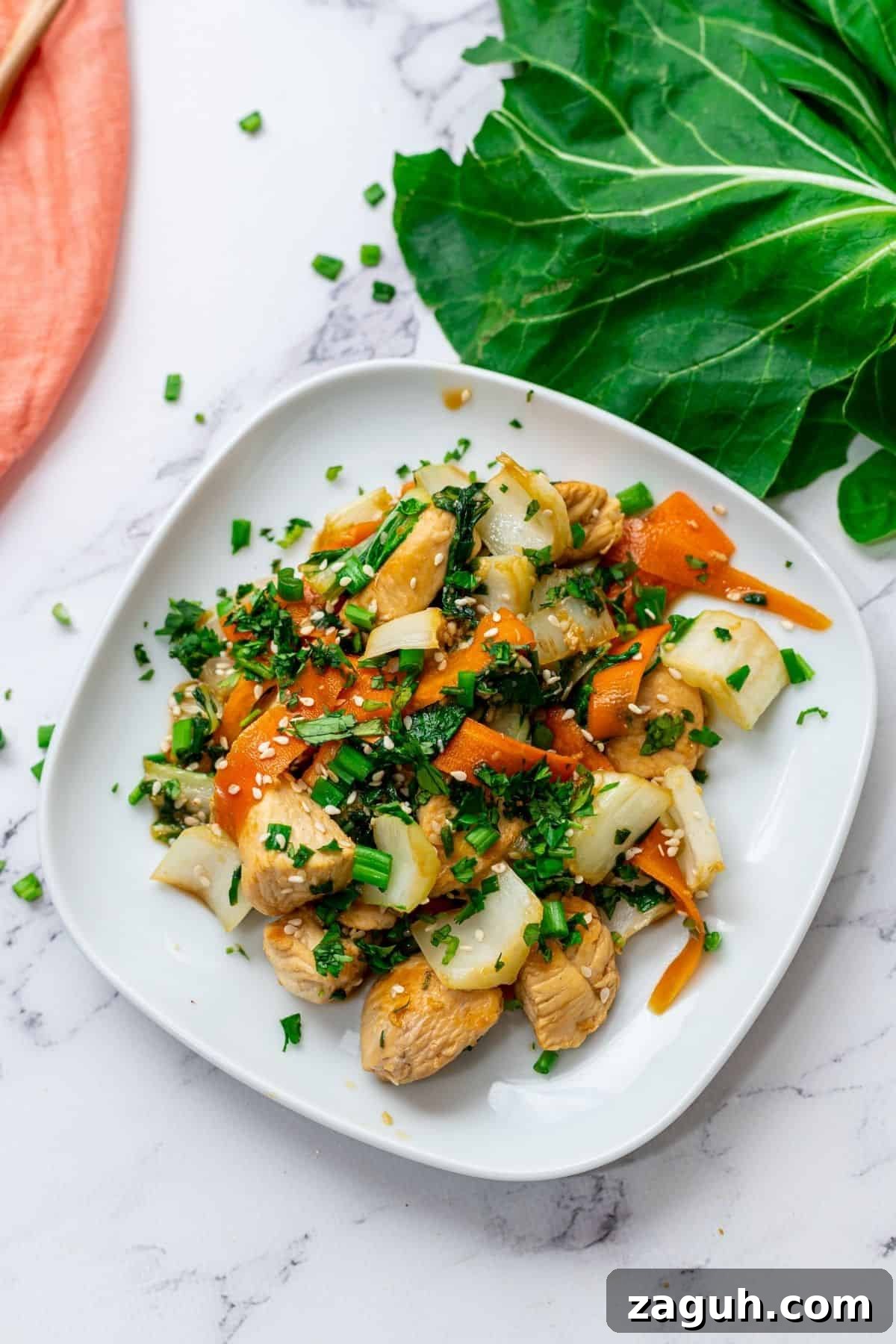 Stir fry with chicken, bok choy, carrots, and a soy honey sauce plated on a white plate topped with sesame seeds.