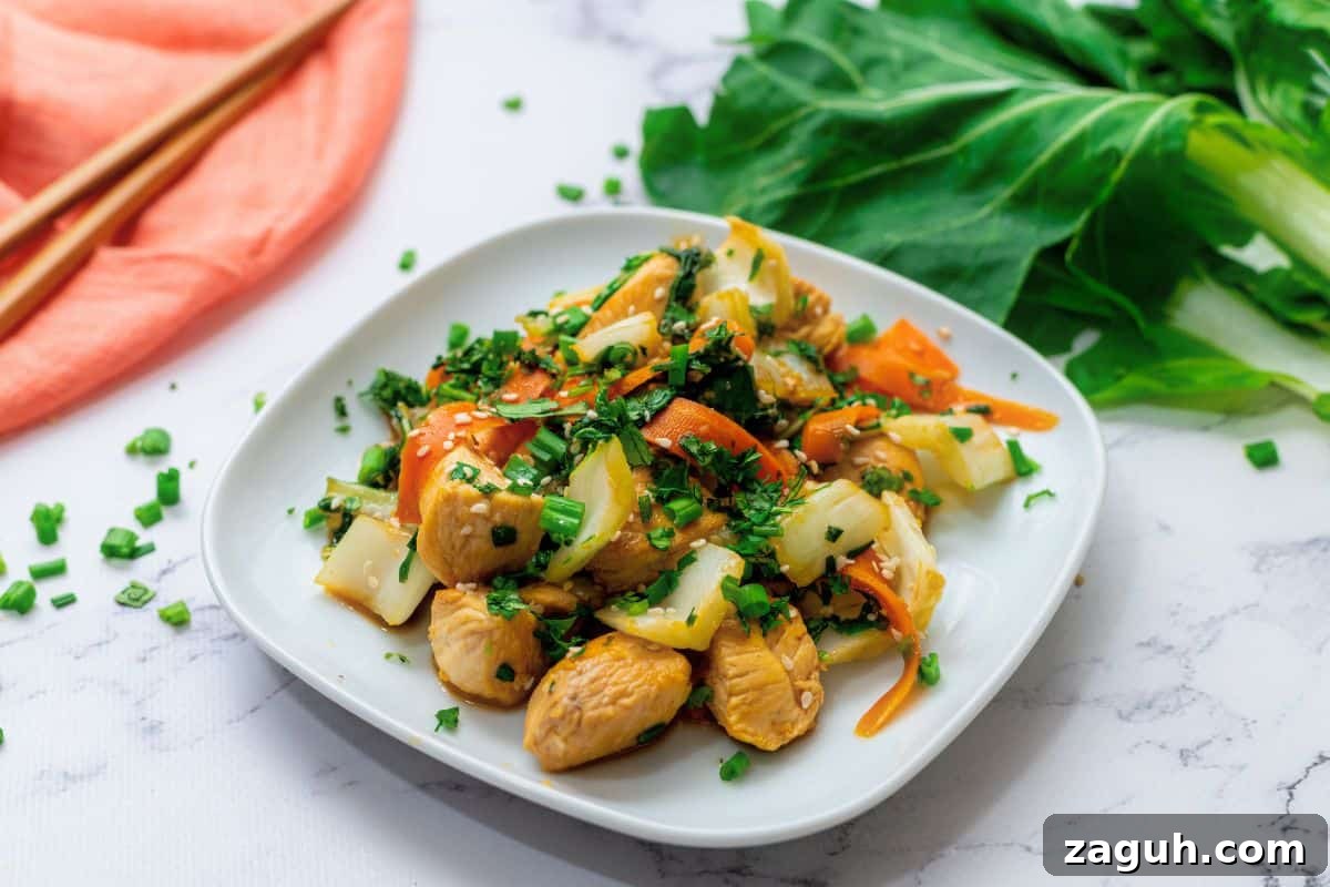 Chicken and bok choy stir fry with carrots and a soy honey sauce on white plate topped with sesame seeds and green onions.