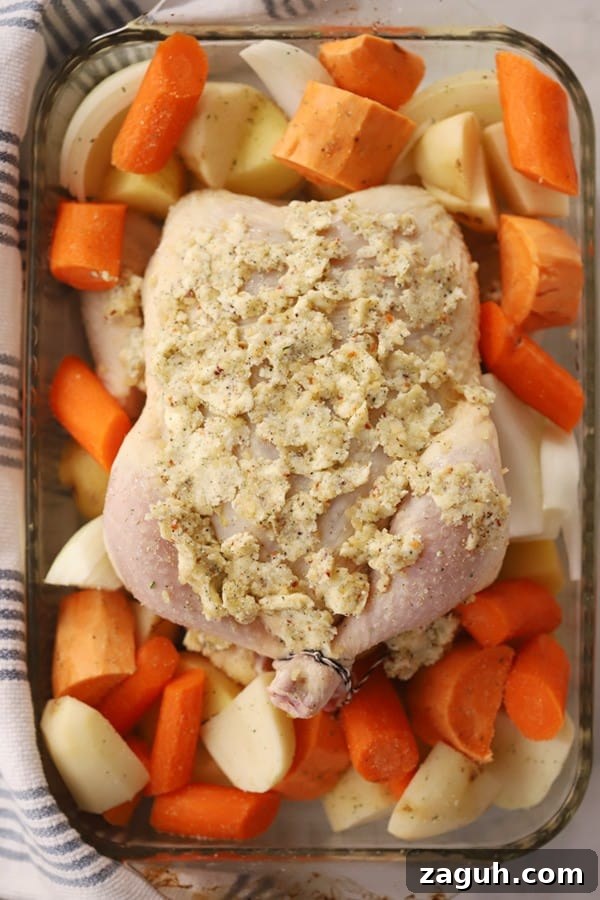 A baking dish with a whole chicken covered in herb butter and surrounded by veggies.