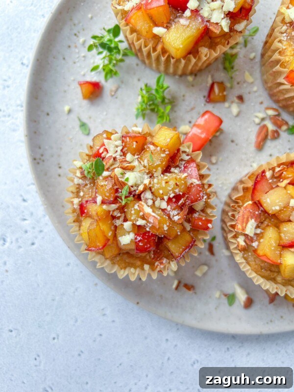 Moist Pumpkin Spice Muffins with Simple Ingredients 11 Overhead view of Almond Flour Blueberry Muffins topped with diced fresh peaches and crushed nuts, arranged on a speckled ceramic plate with a few green herb sprigs scattered around.