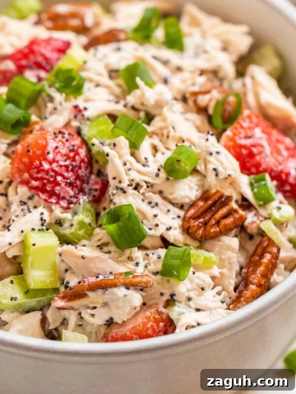 White bowl with strawberry pecan chicken salad topped with green onion and pecans.